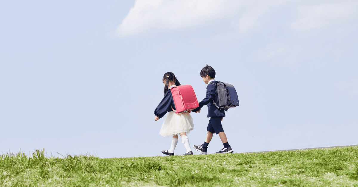 two children in school uniforms with backpacks walking across a field