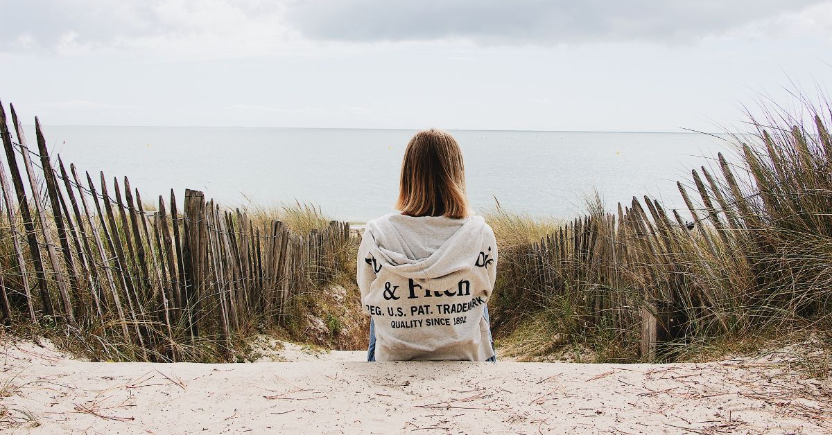 Woman sitting quietly on a beach looking out towards the water
