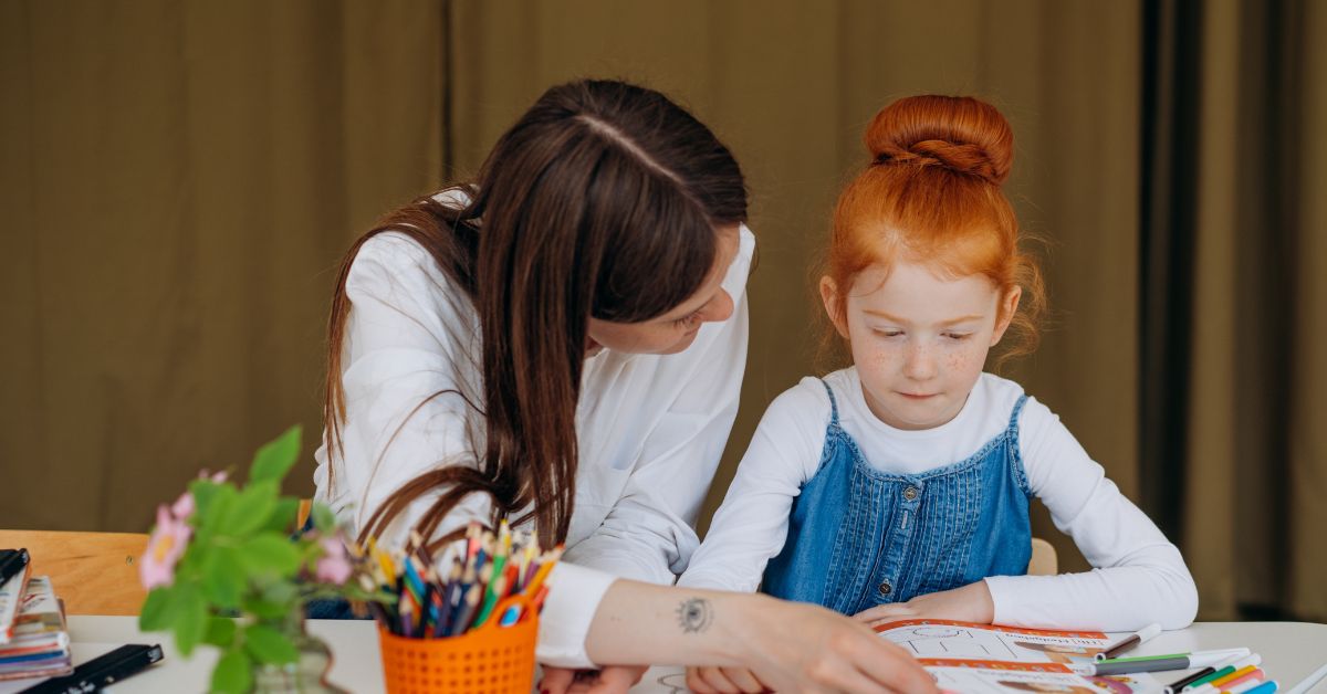 Image is of a female teacher reading with a young student