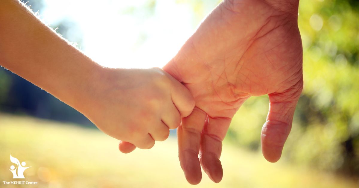 Image is of a child's hand holding the finger of a grown up's hand.