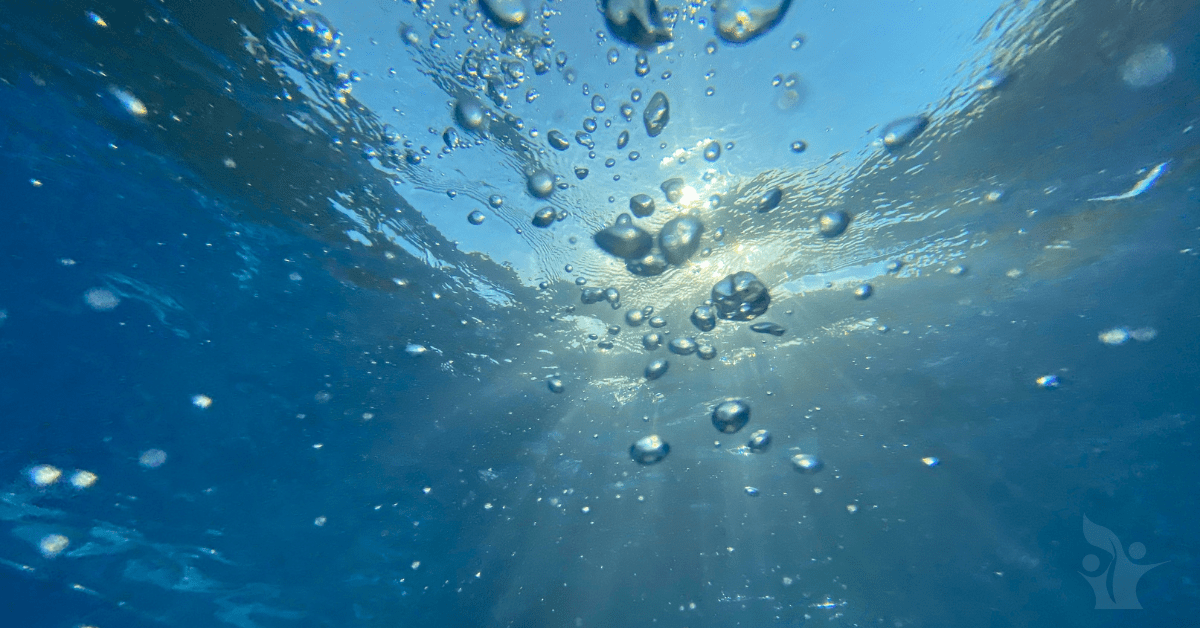 Photograph taken underwater of blue sky and clouds obscured by bubbles coming from under the water