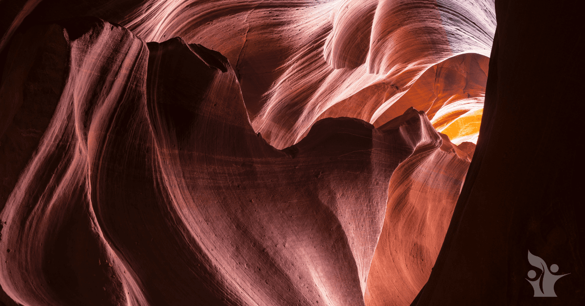 Photograph of a cavern with swirling stone patterns leading to a small exit with light beaming through