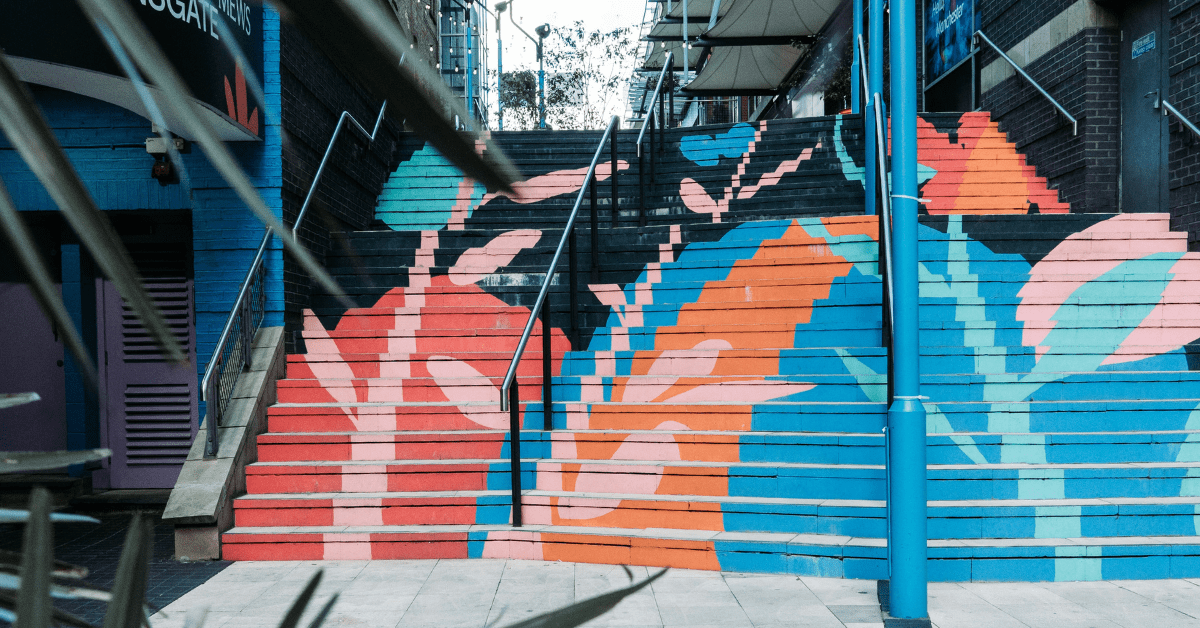 Photograph of city stairs taken from the bottom with brightly coloured abstract flowers in pink, blue, orange and red