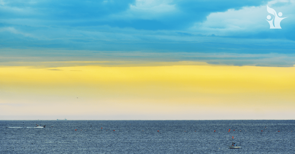 yellow and blue cloudy sky over a kayacker on a calm ocean