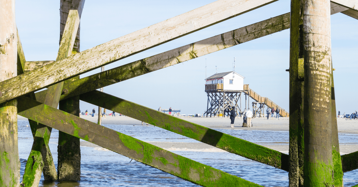 a photo of a family on a beach through the supports of a warf