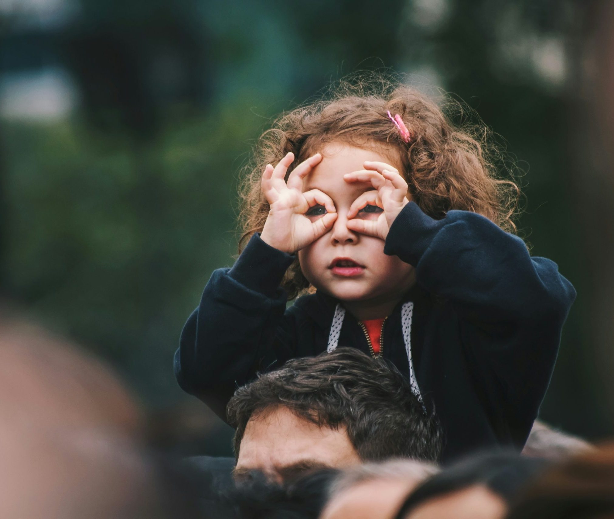 Young child sitting on an adult’s shoulders covering their eyes while seeking connection and support