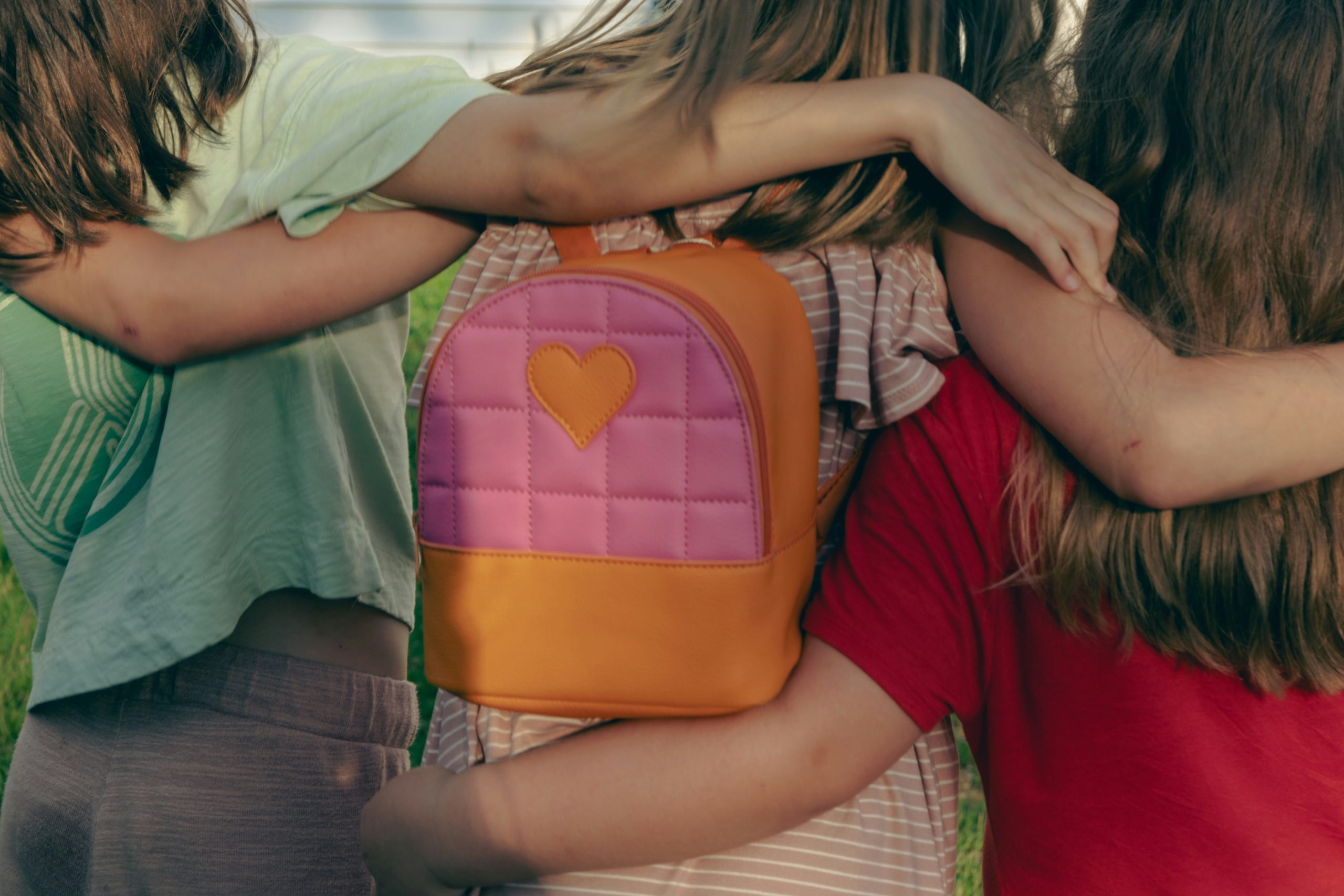 Three students with their arms around each other, standing together outdoors with a backpack visible.