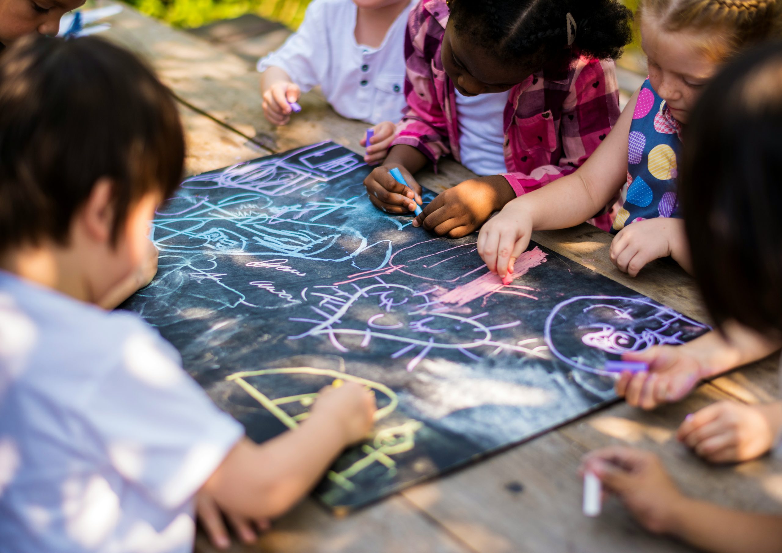 Children collaborate on a large chalk drawing during an outdoor learning activity that encourages creativity, choice, and shared problem-solving.